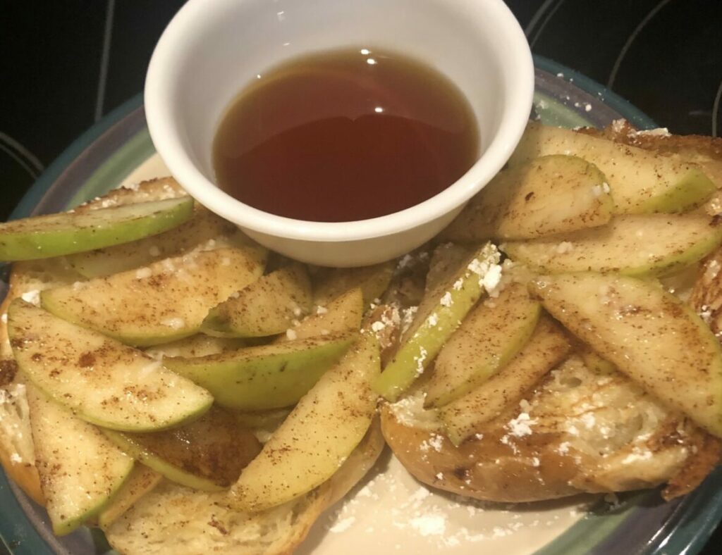 Granny smith apple slices next to a bowl of maple syrup